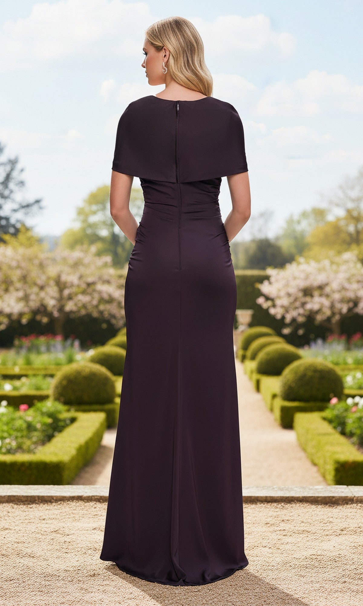 Wearing the La Femme 33157 long prom dress, a woman in a dark purple, floor-length sheath gown with a v-neckline stands outdoors in a formal garden, facing away from the camera.